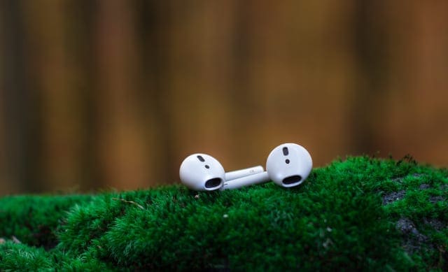 Pair of AirPods on mossy surface outdoors